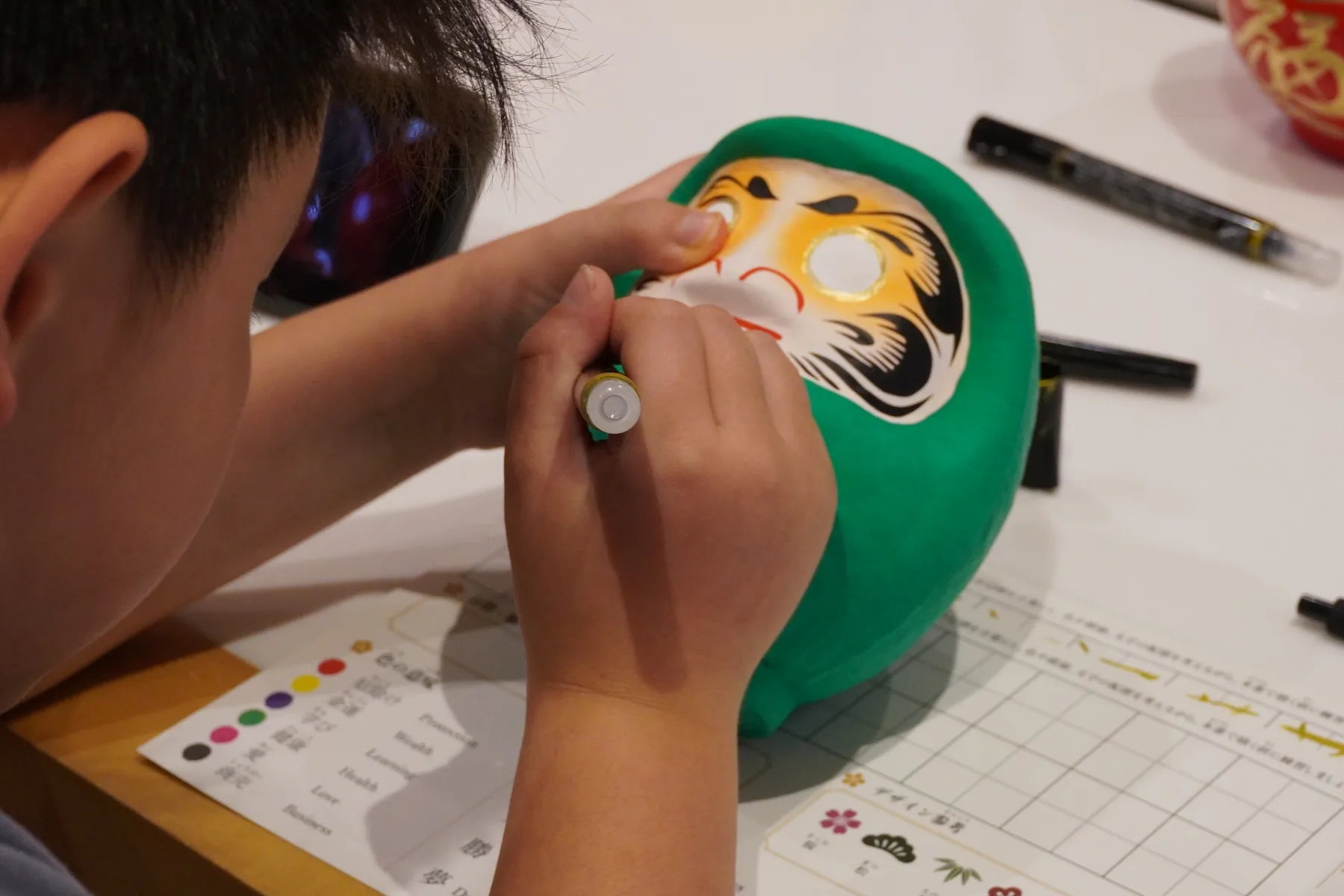 A child finishing a green Takasaki Daruma