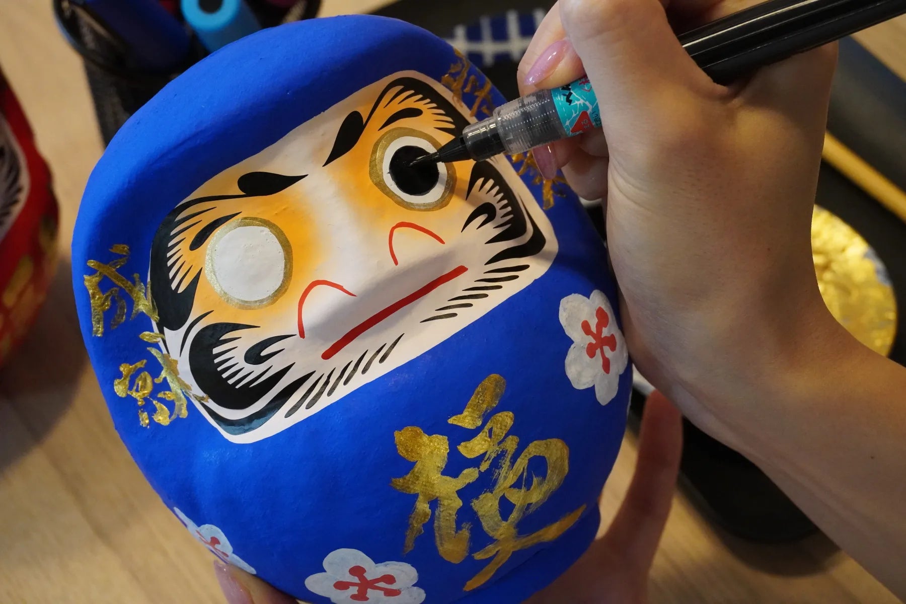 Painting an eye on a blue Takasaki Daruma