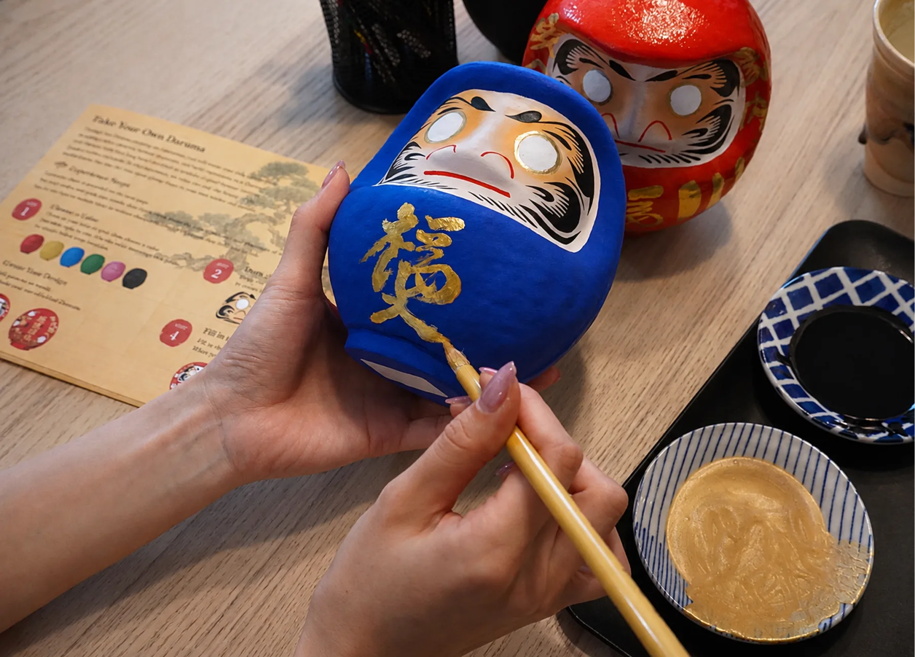 Painting a wish in gold on a blue Takasaki Daruma