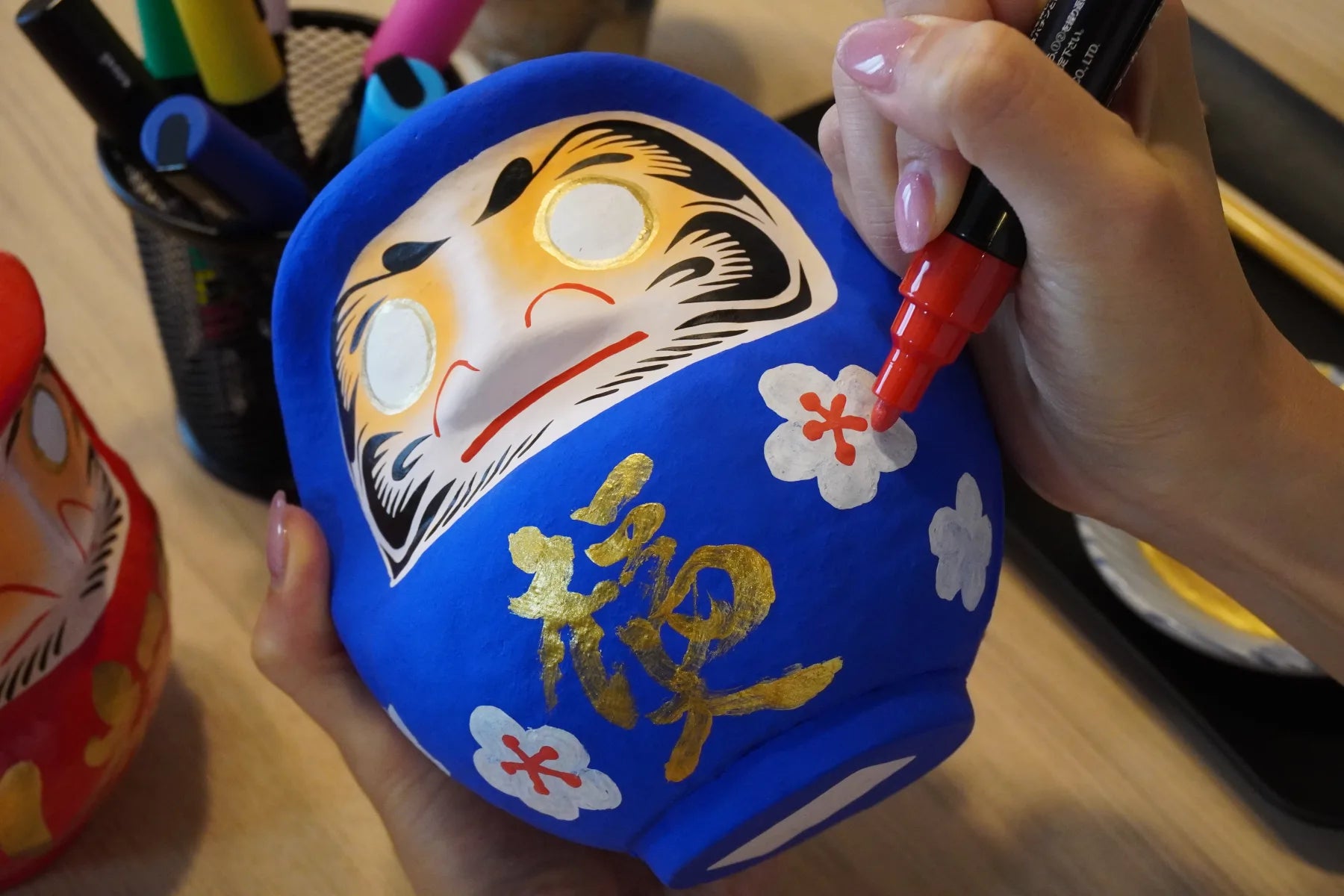 A blue Takasaki Daruma decorated with flowers