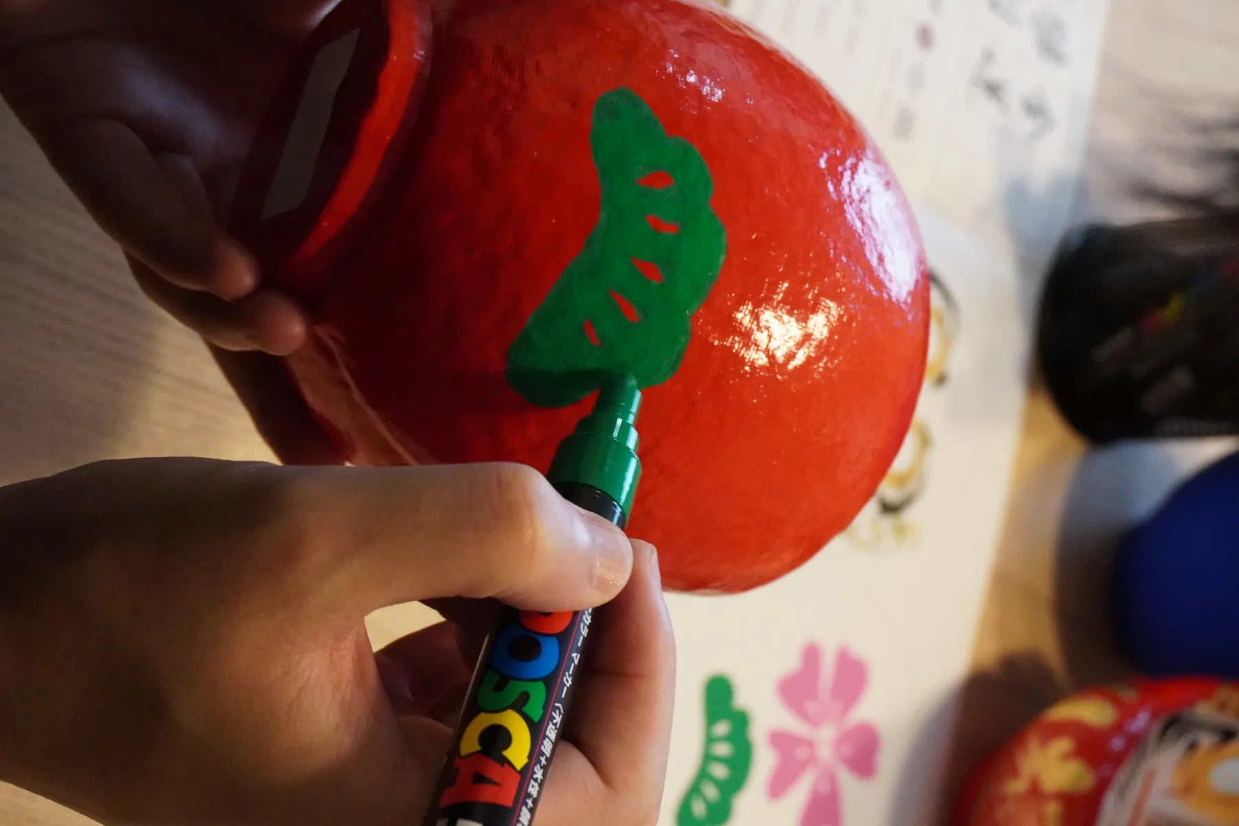 A red Takasaki Daruma decorated with a pine motif